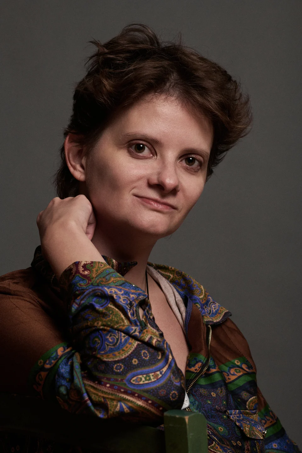 Kate in a patterned shirt, smiling with her chin resting on her hand