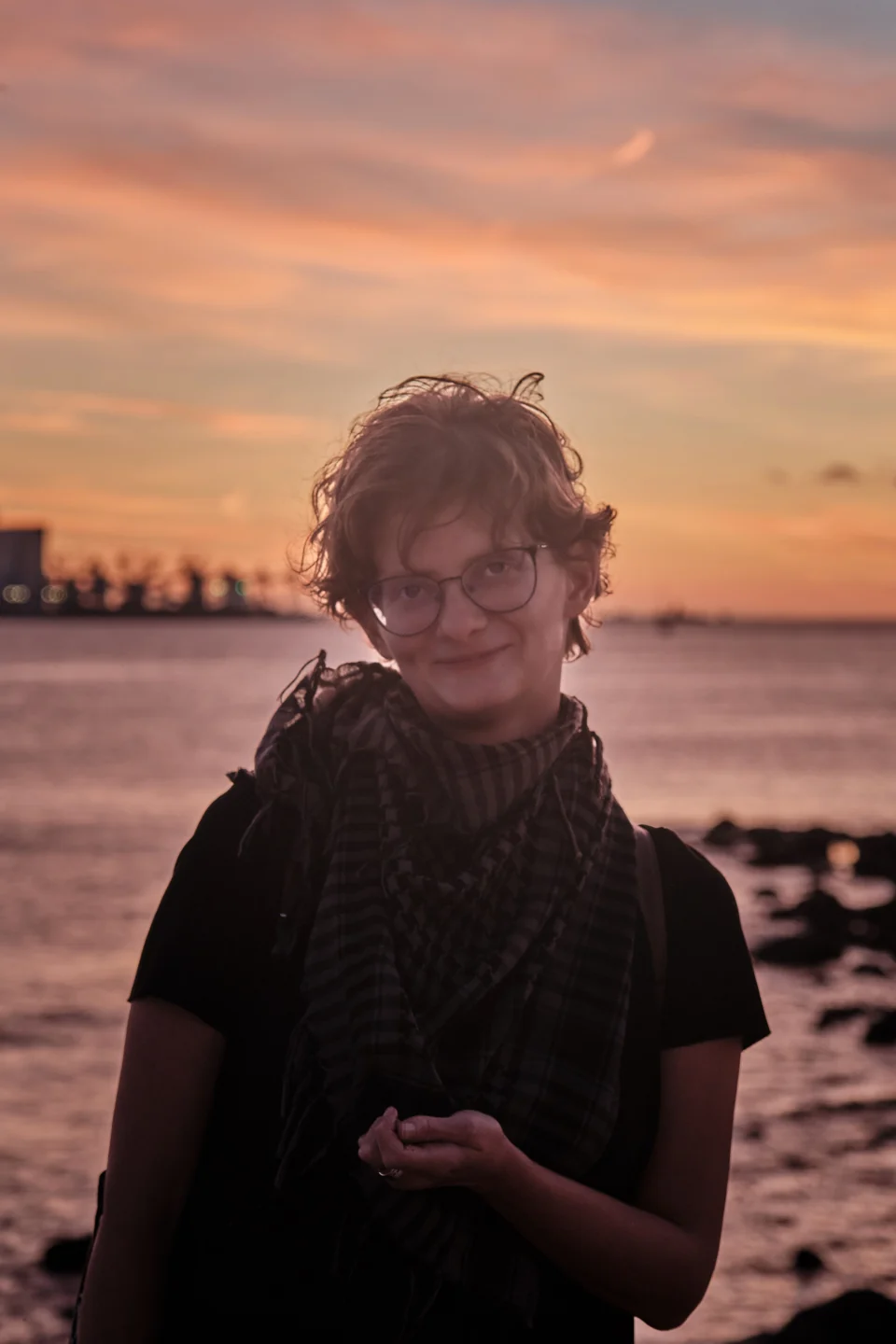 Kate beside the water beneath a pink and orange evening sky
