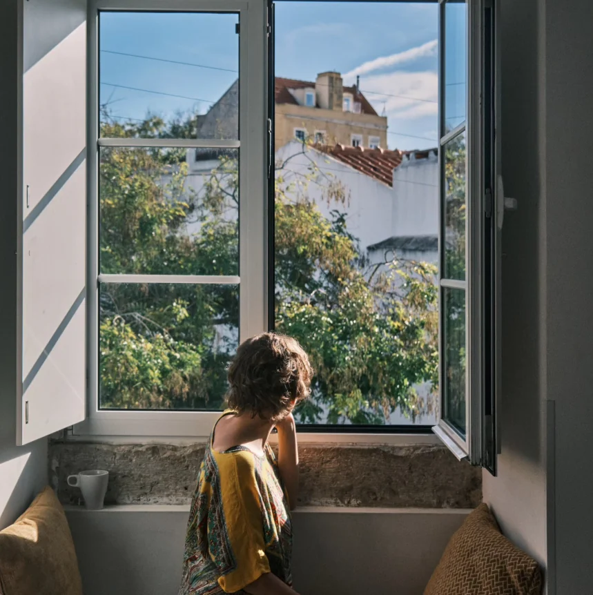 Kate seated by an open window overlooking trees and tiled rooftops